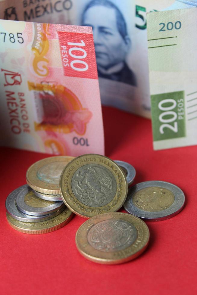 Monedas mexicanas y billetes de diferente denominación sobre el fondo rojo. foto