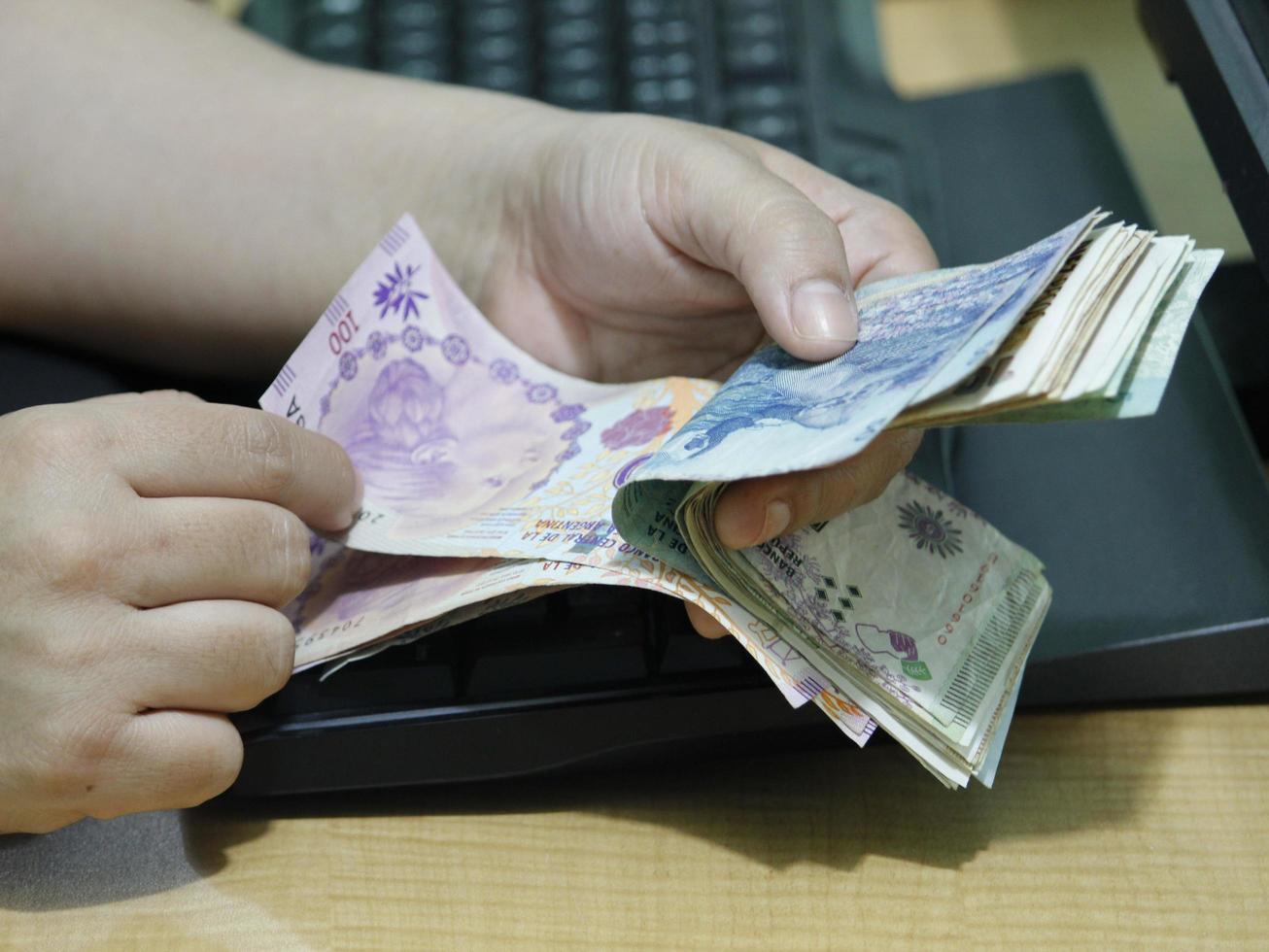 Hands of a woman counting Argentine money on a computer keyboard photo