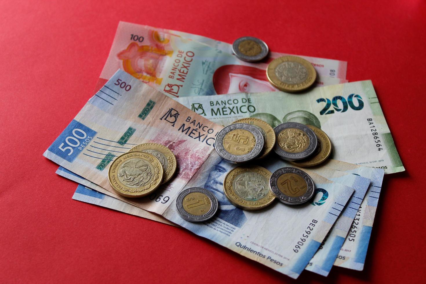 Monedas mexicanas y billetes de diferente denominación sobre el fondo rojo. foto