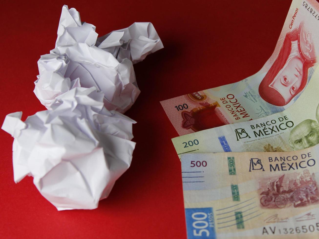 Crumpled sheets of paper and Mexican bills on red background photo