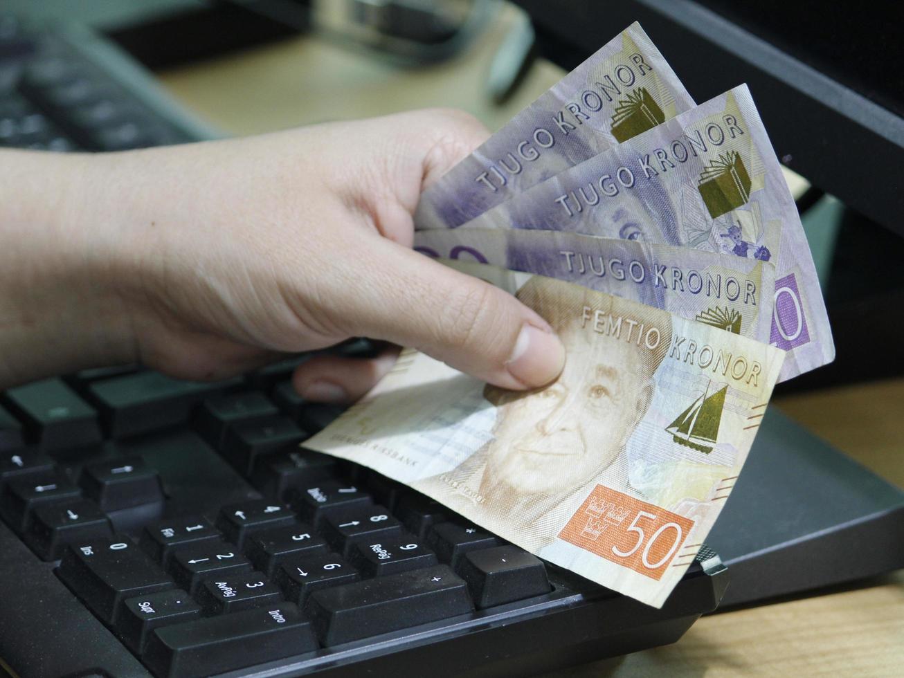 Mano de una mujer sosteniendo dinero sueco en un teclado de computadora foto