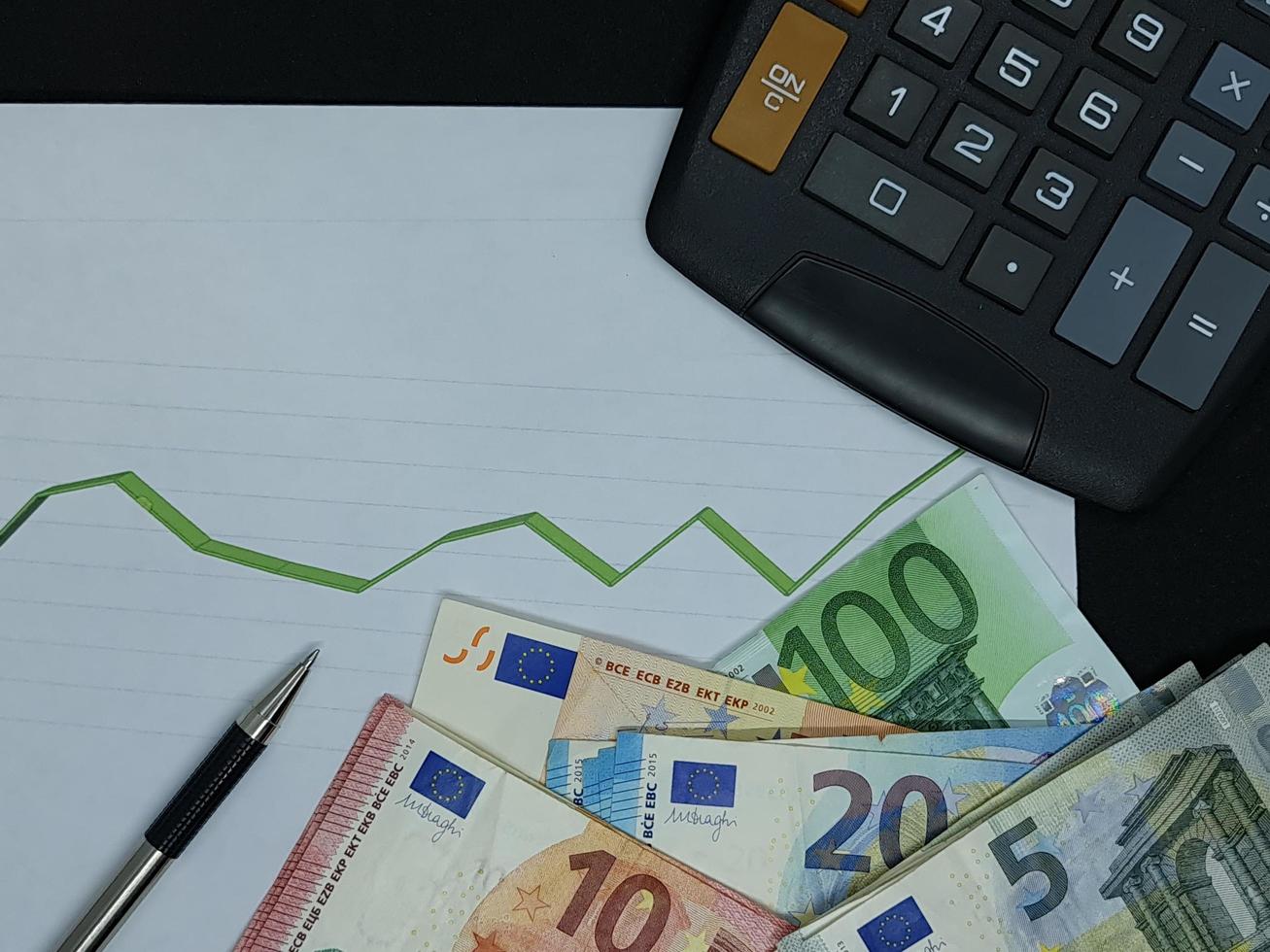 European banknotes, pen and calculator on background with rising trend green line, view from above photo