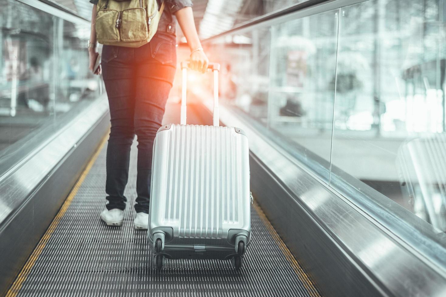 Vista posterior de la mujer de belleza viajando y sosteniendo la maleta en la escalera mecánica foto