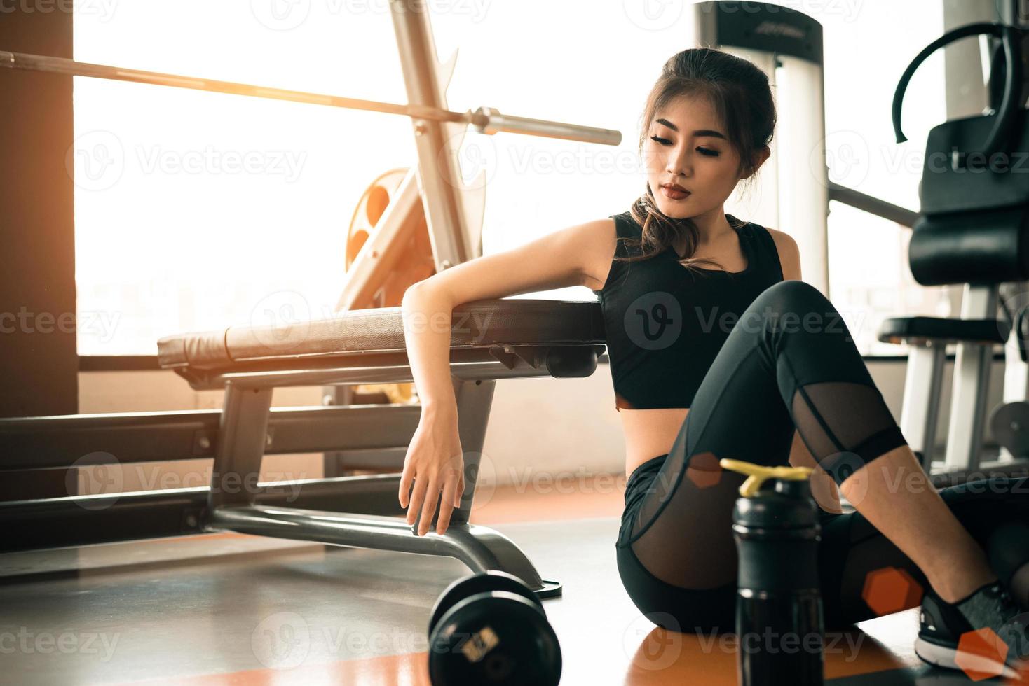 Asian young woman relaxing in fitness gym and sport club center with equipment and dumbbell. Workout and Strength training concept. Beauty and Healthy theme. Gymnasium background photo