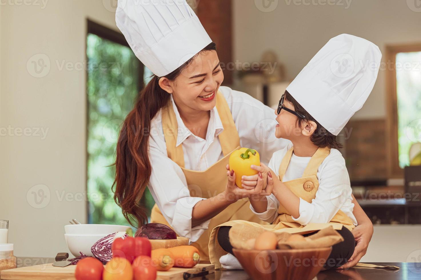 Happy Asian family in kitchen. Mother and son in chef hat preparing food in home kitchen together. People lifestyle and Family. Homemade food and ingredients concept. Two Thai people in teaching class photo