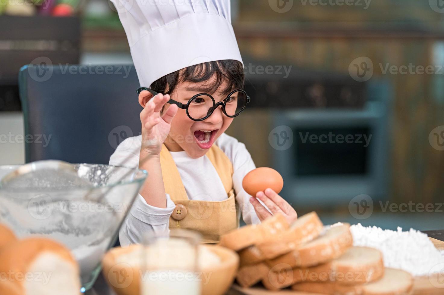 Portrait cute little Asian happy boy surprised and interested in cooking funny in home kitchen. People lifestyles and Family. Homemade food and ingredients concept. Baking Christmas cake and cookies photo