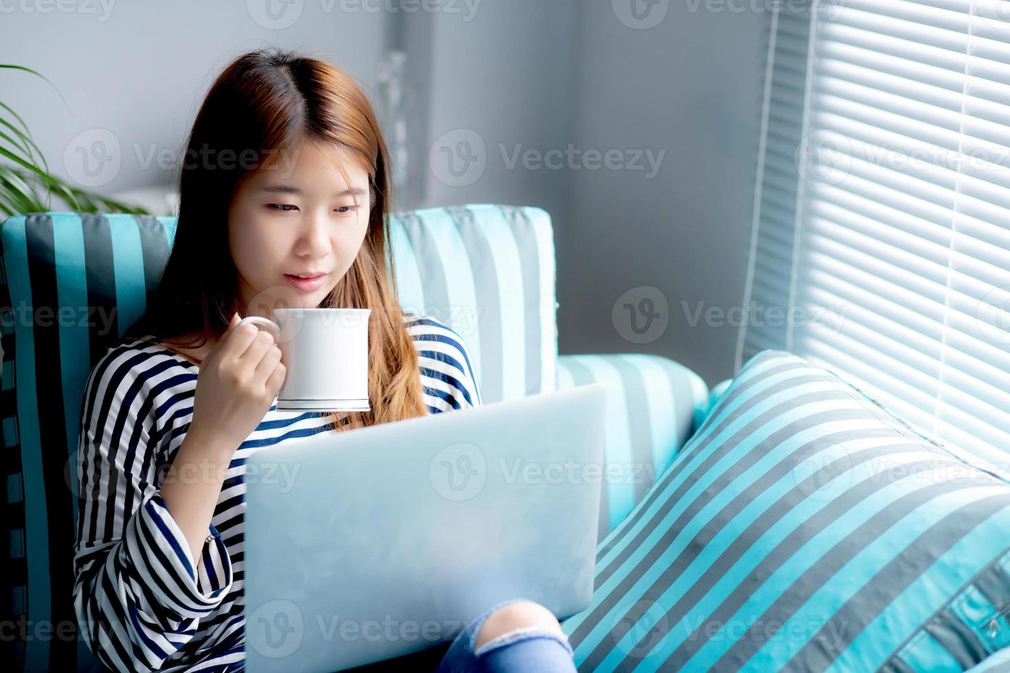 mujer asiática joven que se sienta usando en la computadora portátil y tomar café. foto