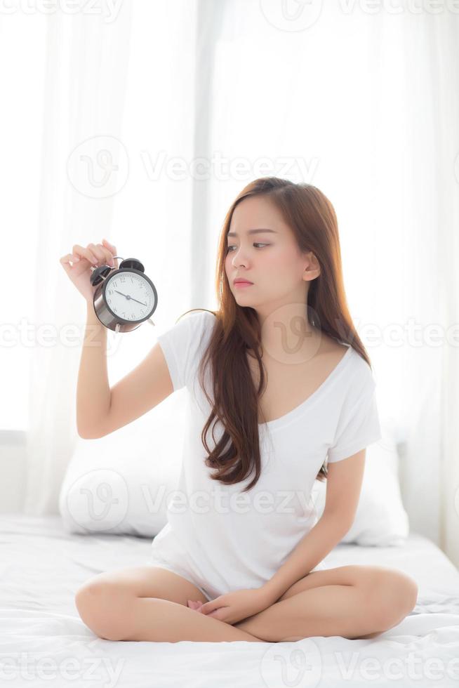 joven mujer asiática se despierta en la mañana molesto despertador de la mano. foto