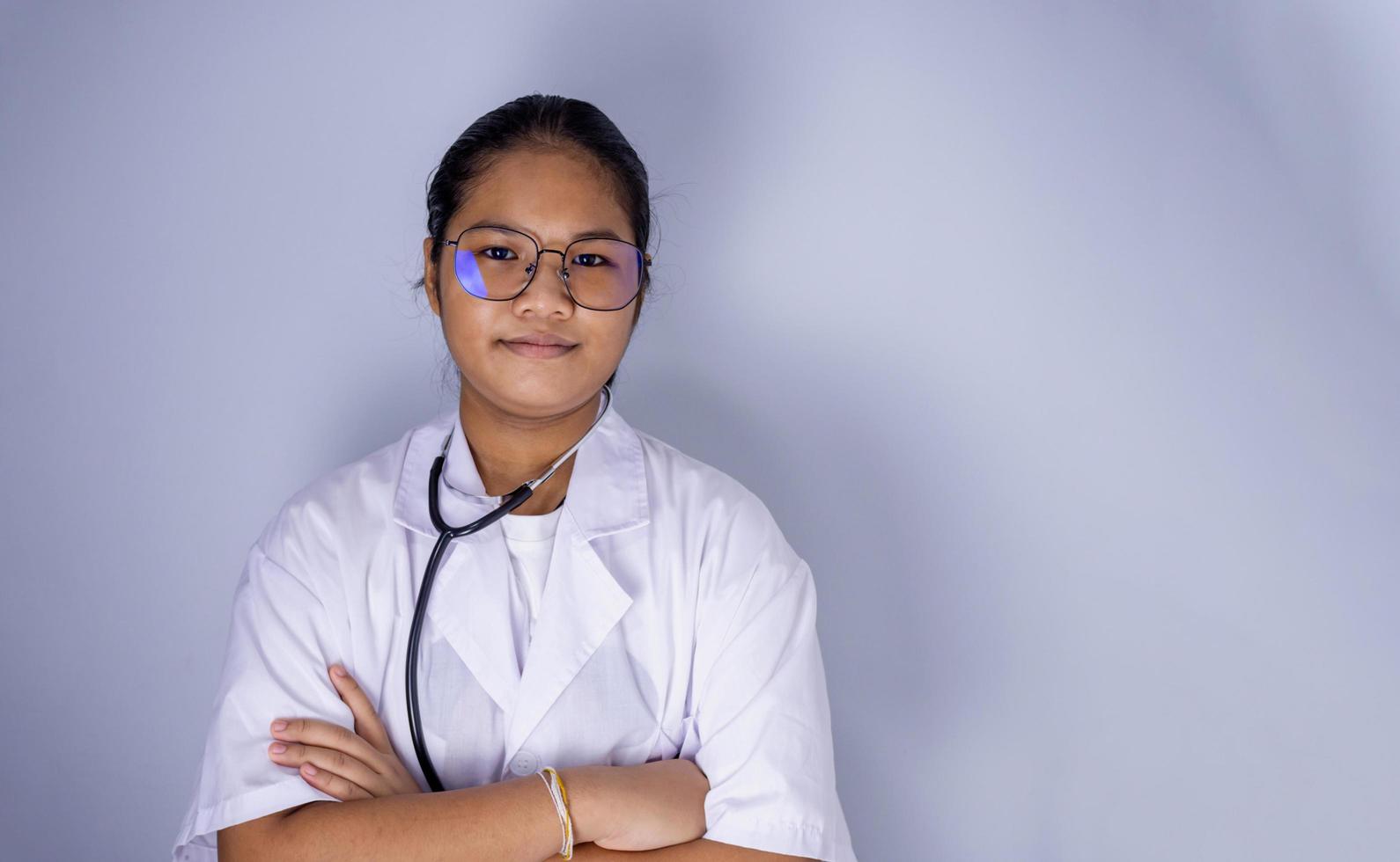 Retrato de una doctora con gafas de pie con los brazos cruzados sobre un fondo blanco. foto