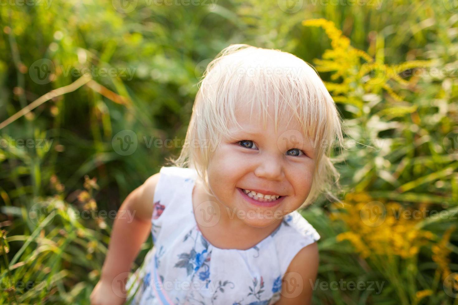 Little girl in summer dress looks into a camera photo