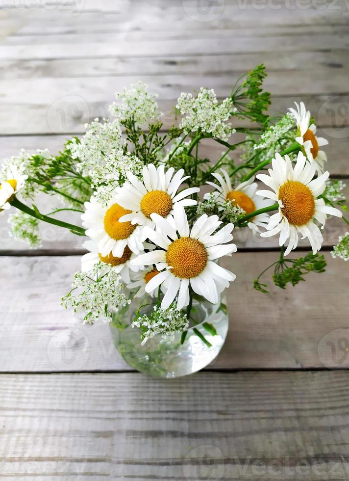 Field daisies on a wooden background. Chamomile flower in a glass vase. View from above. Beautiful summer still life. photo