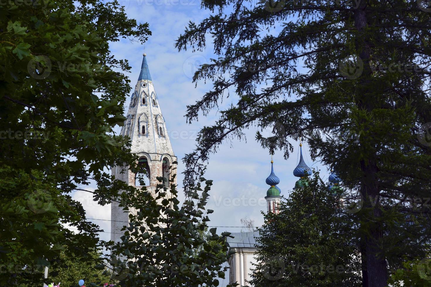 cúpulas de la iglesia con cruces contra el cielo azul. templo de piedra blanca entre los árboles del pueblo. foto