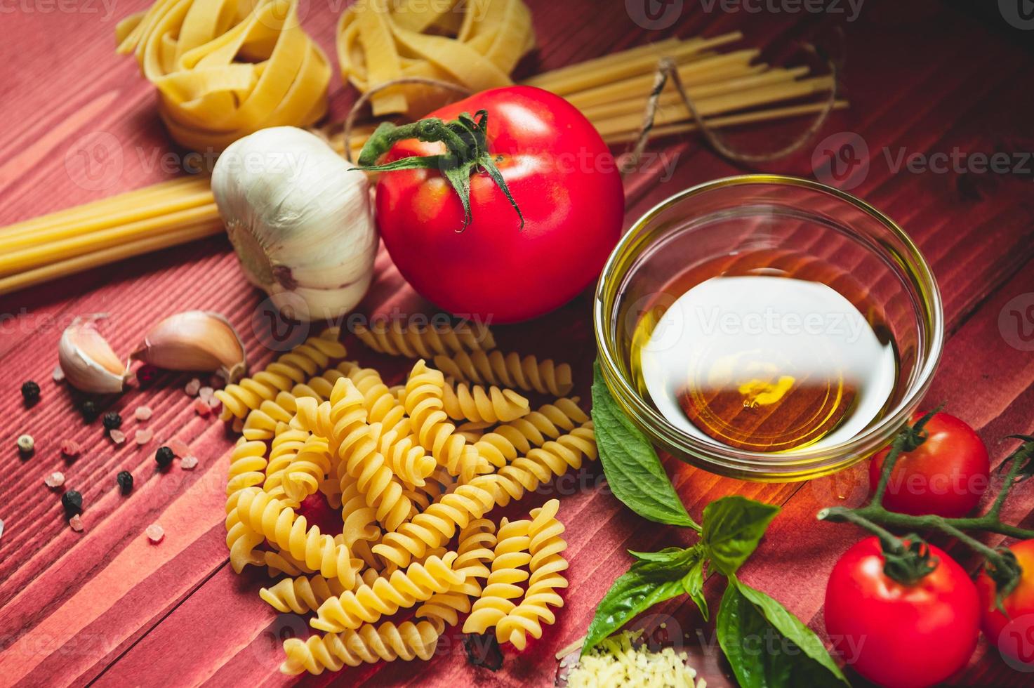 Sabrosos y apetitosos ingredientes de pasta de espagueti italianos para la cocina de la cocina con tomate, queso parmesano, aceite de oliva, fettuccine y albahaca en la mesa de madera marrón. comida italiana receta casera. vista superior foto