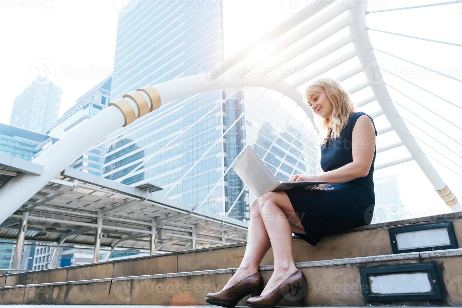 mujer de negocios que trabaja con la computadora portátil al aire libre. concepto de tecnología y felicidad. concepto de belleza y estilo de vida. ciudad y tema urbano. mujer de cabello rubio usando computadora foto