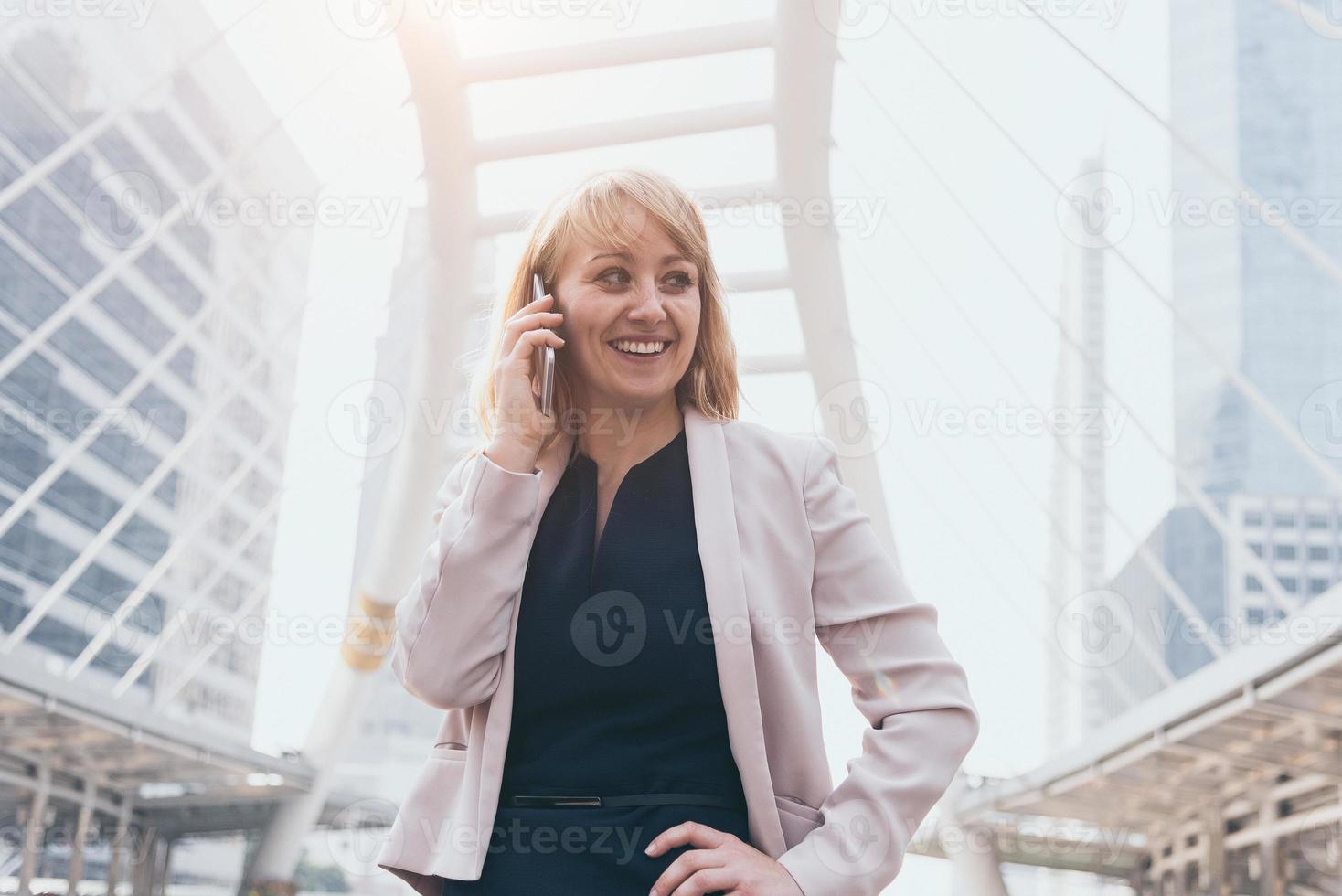 Happy businesswoman using smart phone to communicate and talk to business agreement in urban city background. People lifestyles and technology concept. Outdoor working and social distancing concept photo