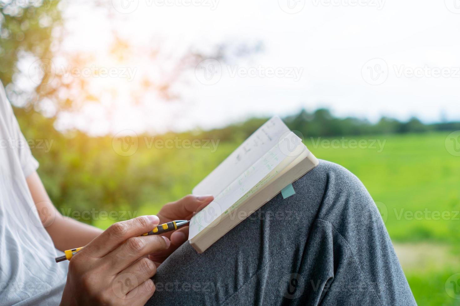 In a public park, a man is handwriting in a small white memo pad to make a note of something he doesn't want to forget or to make a to-do list for the future. photo