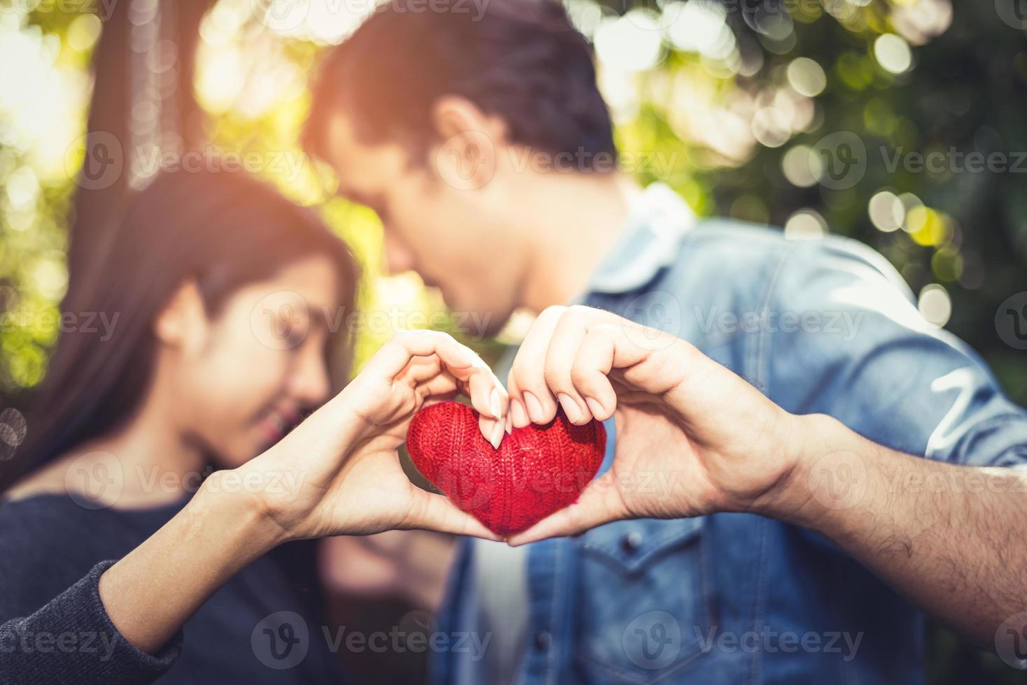 Two hands of young lovers or couple holding Red Heart yarn in middle at natural outdoor background for Valentines day. Holiday and relax concept. Honeymoon Celebration Party and Wedding Anniversary photo