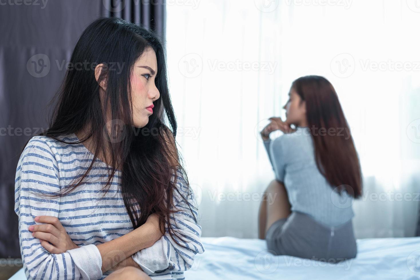 Asian woman having stressed after conflict with girlfriend in bedroom. Serious and negative thinking people. Upset and unhappy female concept. Lifestyle and family issues. LGBT theme photo