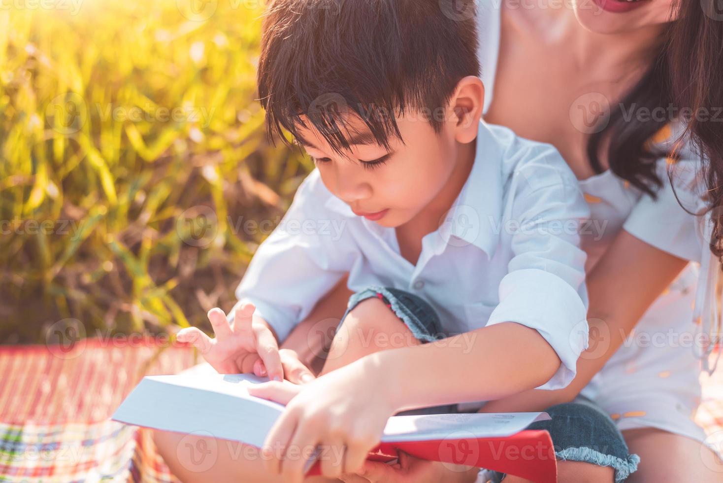 niño asiático y su madre leyendo libros de cuentos en el campo del prado. madre e hijo aprendiendo juntos. celebrando el día de la madre y apreciando el concepto. gente de verano y educación de estilo de vida. foto