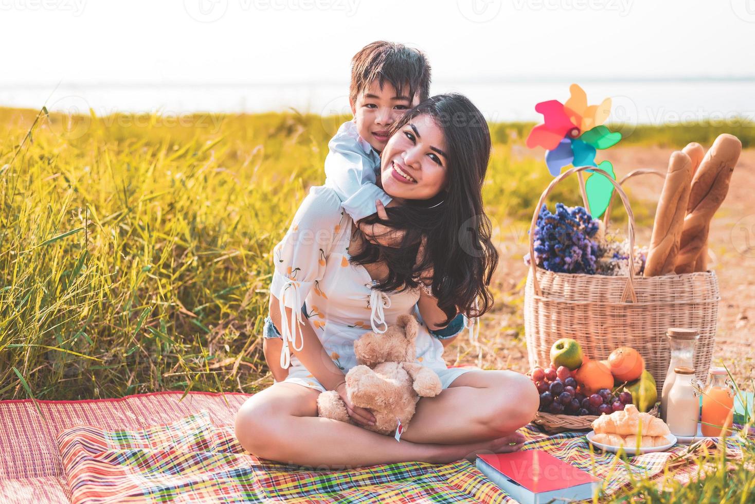 Beautiful Asian mother and son doing picnic and in Easter summer party on meadow near lake and mountain. Holiday and Vacation. People lifestyle and Happy family life concept. Thai person photo