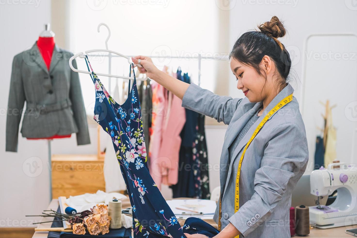 Muchacha asiática del diseñador de moda femenina que hace el diseño de la nueva ropa azul hermosa del vestido con la percha en el estudio. sala de exposición con estilo diseñador de moda. concepto de costura y sastre. estilista modista creativa foto