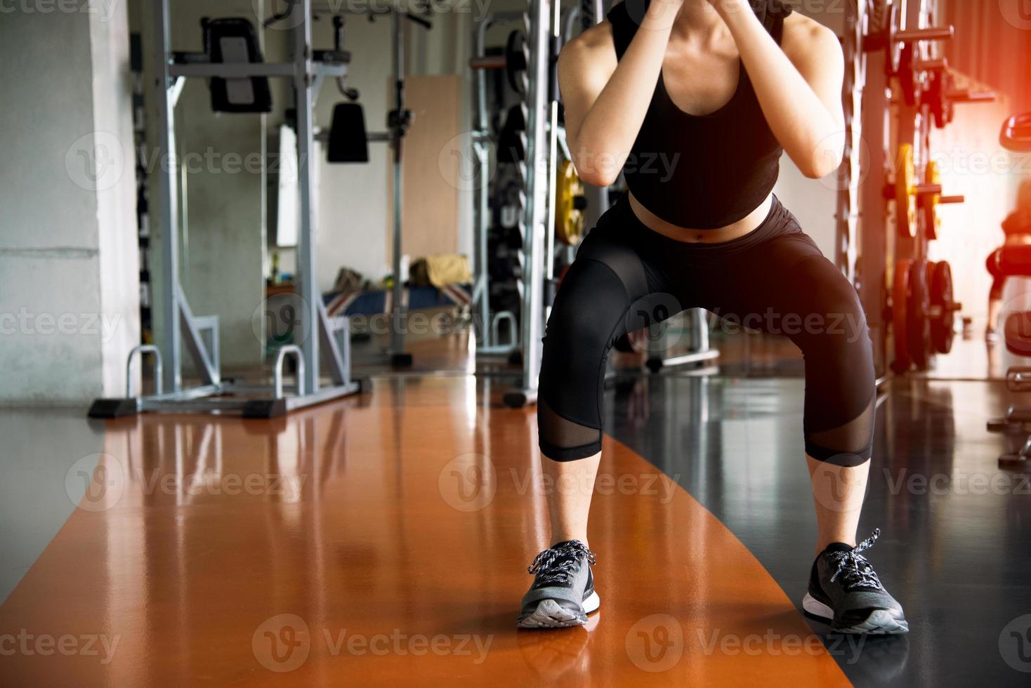 Mujer fitness haciendo ejercicios en cuclillas para quemar grasa y fortalecer las piernas en el gimnasio deportivo con equipamiento deportivo en segundo plano. la belleza y el cuerpo construyen el concepto. club deportivo y tema aeróbico. foto