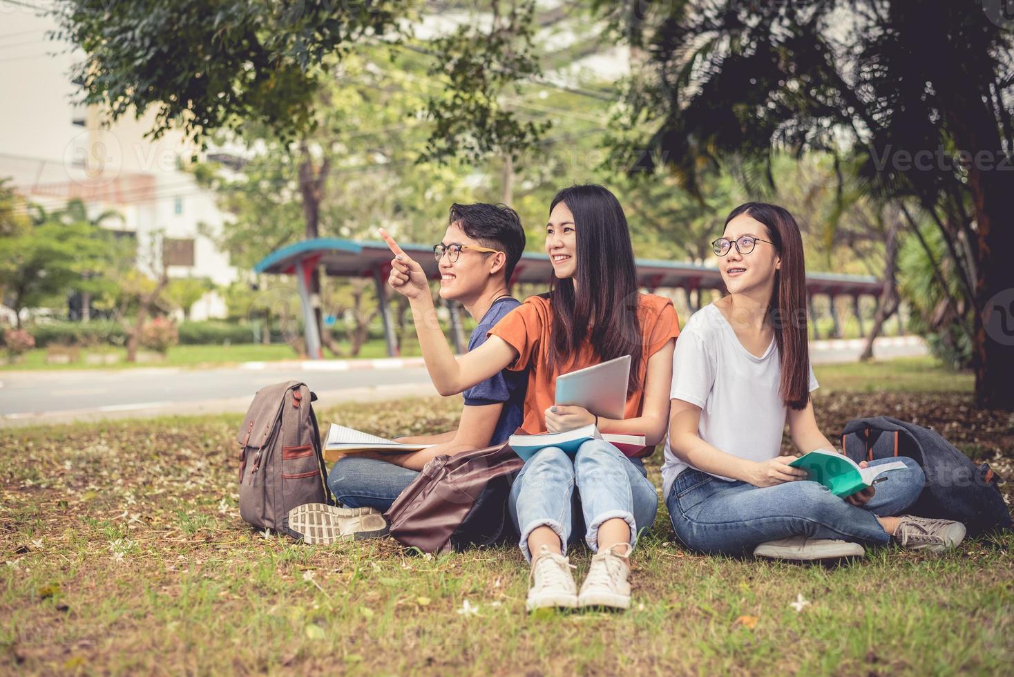 Group of Asian college student reading books and tutoring special class for exam on grass field at outdoors. Happiness and Education learning concept. Back to school concept. Teen and people theme photo