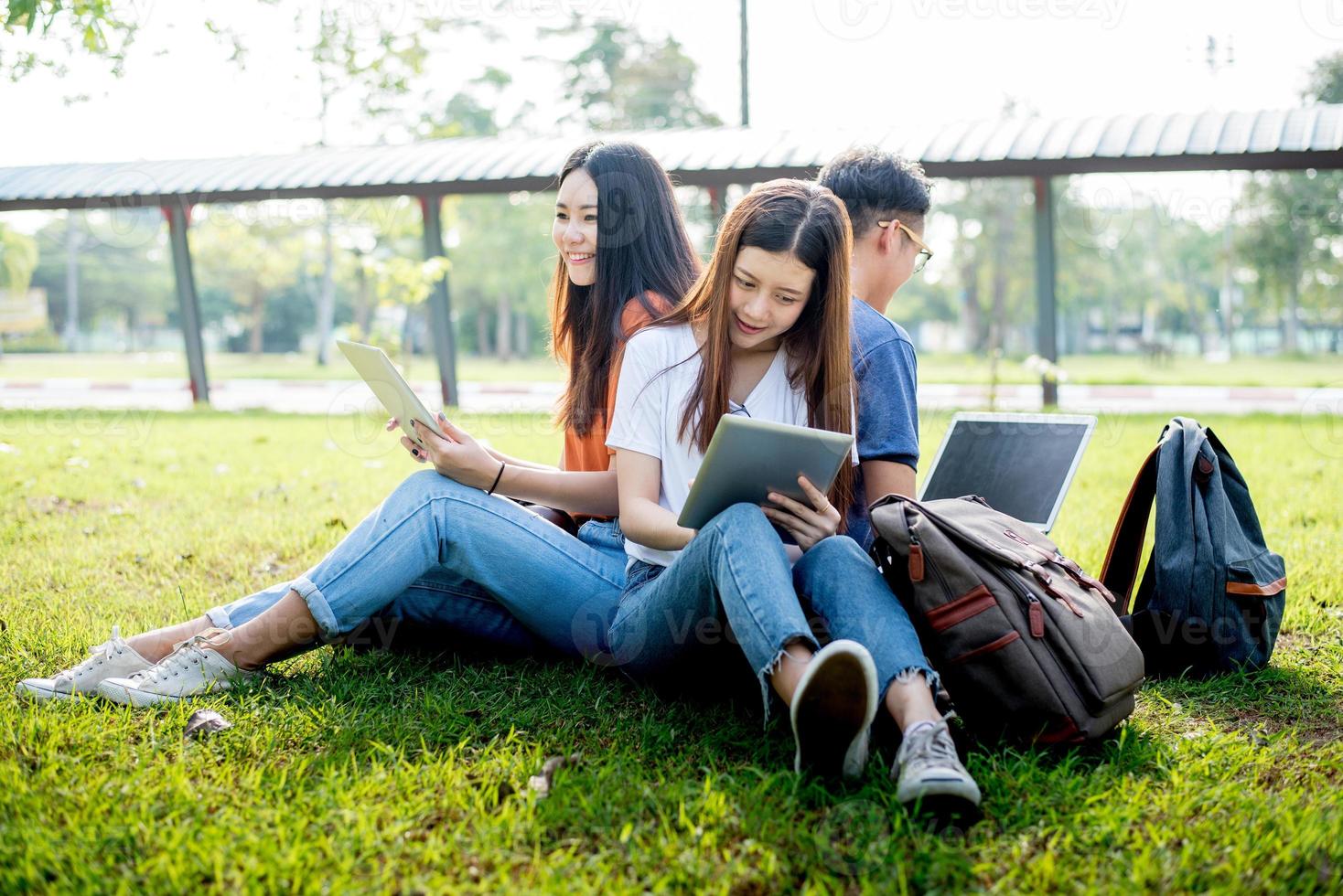 Group of Asian college student using tablet and laptop on grass field at outdoors. Technology and Education learning concept. Future Technology and Modern entertainment concept. Edutainment theme photo