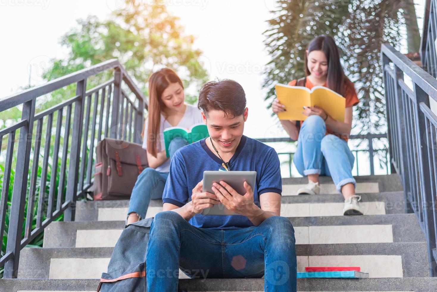 Grupo de estudiantes universitarios asiáticos leyendo y revisando libros de texto y una computadora portátil en la escalera de la universidad. concepto de aprendizaje de tecnología y educación. tema de entretenimiento y entretenimiento educativo foto