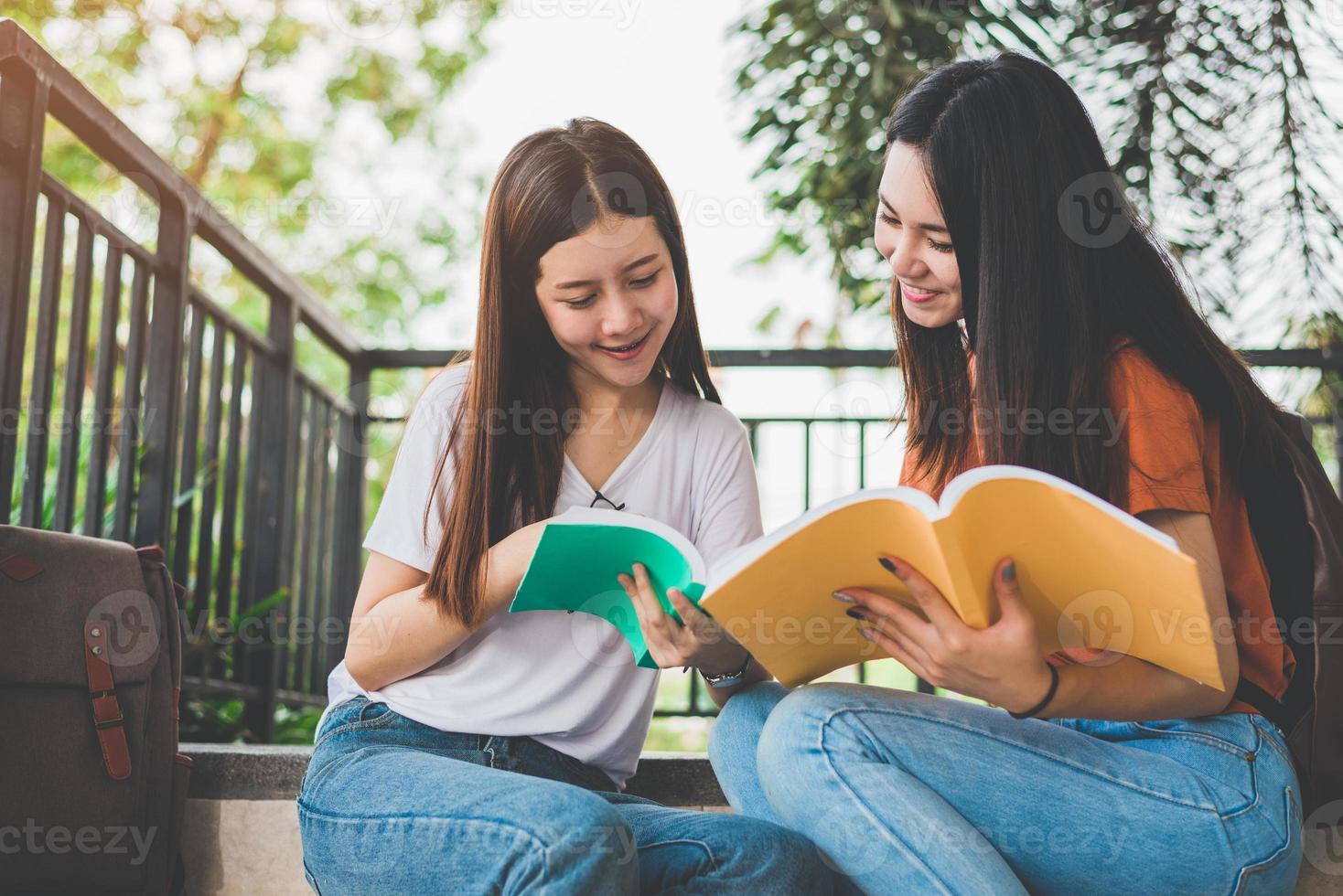 Two Asian beauty girls reading and tutoring books for final examination together. Student smiling and sitting on stair. Education and Back to school concept. Lifestyles and People portrait theme photo