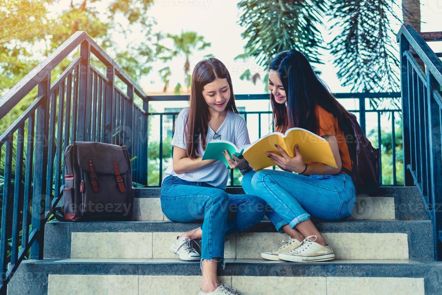 Two Asian beauty girls reading and tutoring books for final examination together. Student smiling and sitting on stair. Education and Back to school concept. Lifestyles and People portrait theme photo