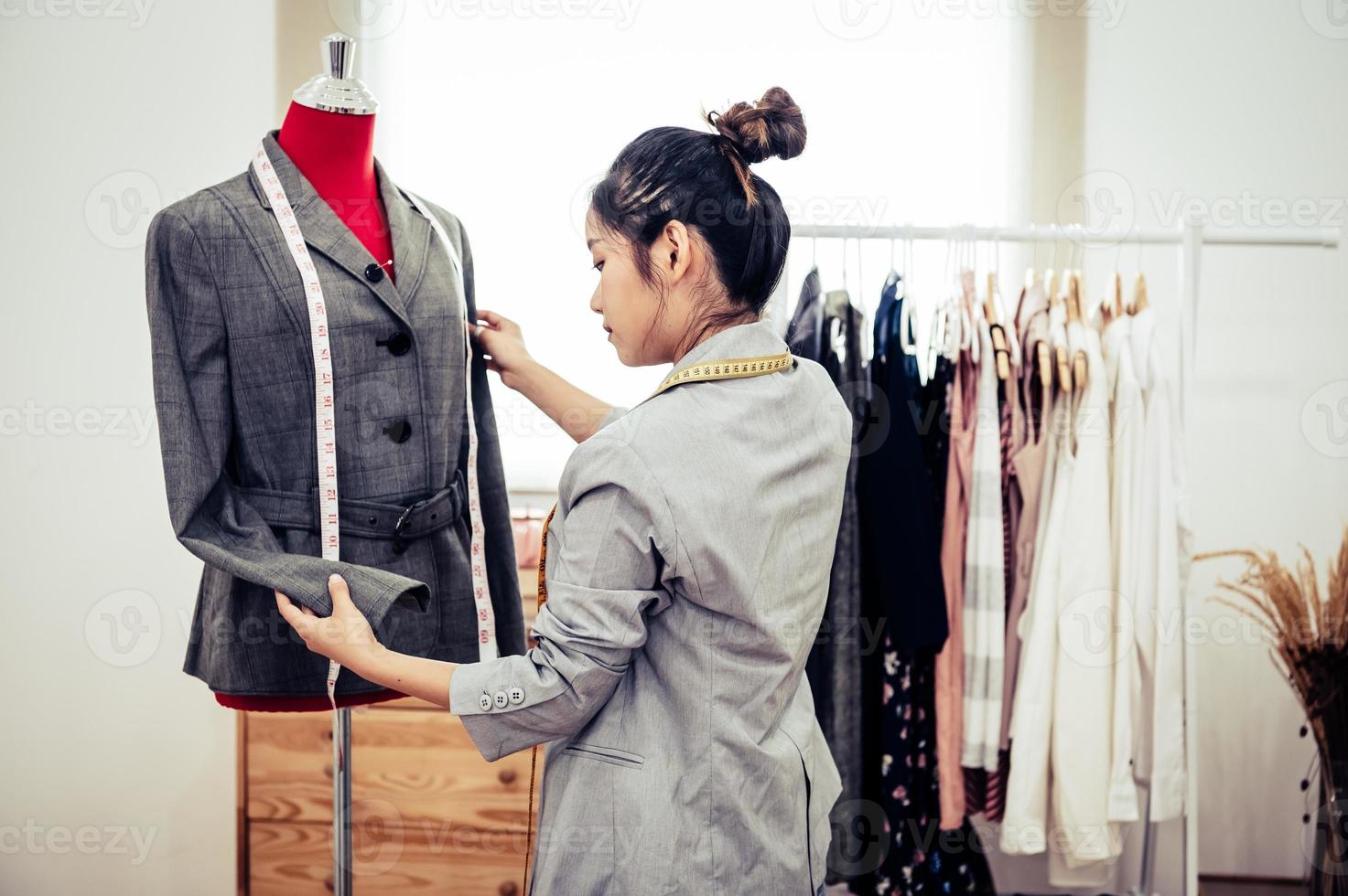 Chica asiática diseñadora de moda femenina que encaja en la ropa de uniforme de traje formal en modelo de maniquí. sala de exposición con estilo diseñador de moda. concepto de costura y sastre. estilista modista creativa foto