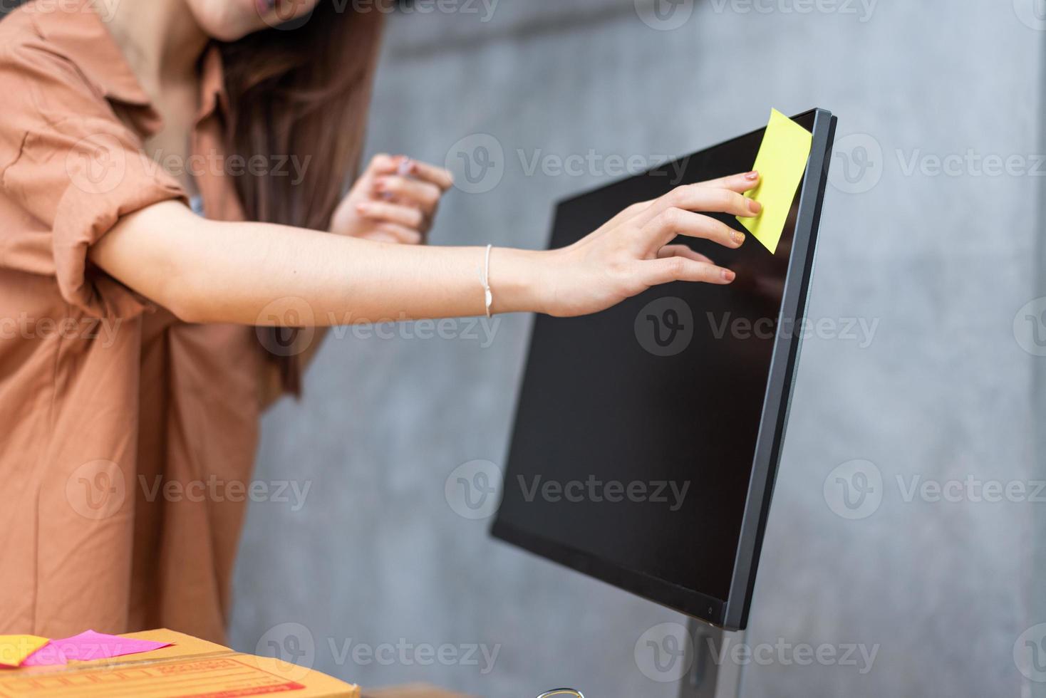 Business woman sticking order list memo on computer screen for reminding to send parcels to customers. Business and Service concept. Online shopping and Small business entrepreneur theme photo