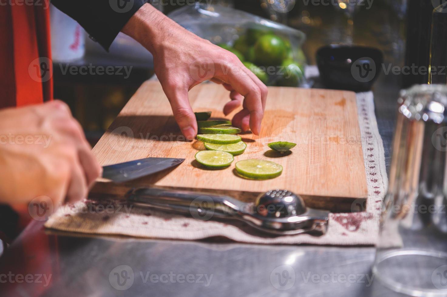 Closeup of professional bartender hand slicing lemon for making lemonade juice by knife in night club. Chef making drinks for guest in pub restaurant. Food and beverage concept photo