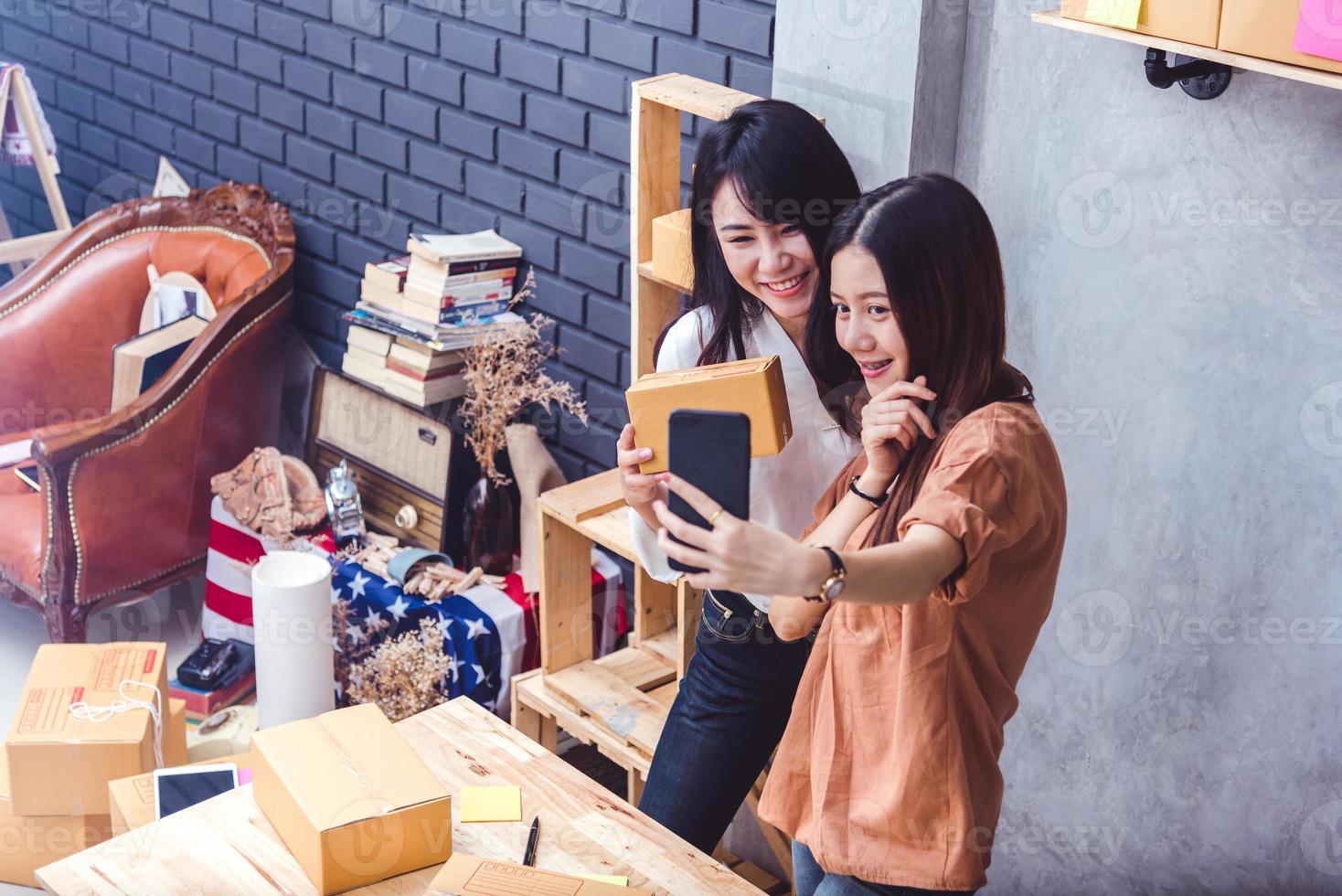 Two women took a selfie by mobile phone while selling online together. Business and people lifestyles concept. Thai girls take a photo while online shopping