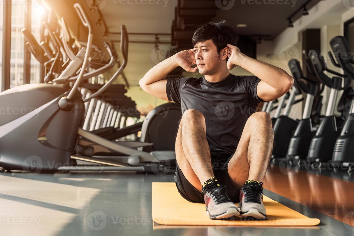 hombre de deporte haciendo abdominales o sentadillas posturas sobre estera de yoga en el gimnasio en condominio con fondo de equipos de gimnasia. Gente de trabajo de oficina estilos de vida y concepto de entrenamiento deportivo foto