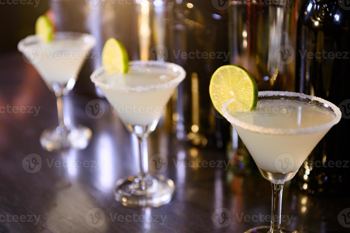 Closeup of lemonade drinks in martini glasses on bar in night club. Close up alcohol in pub restaurant. Food and beverage concept photo