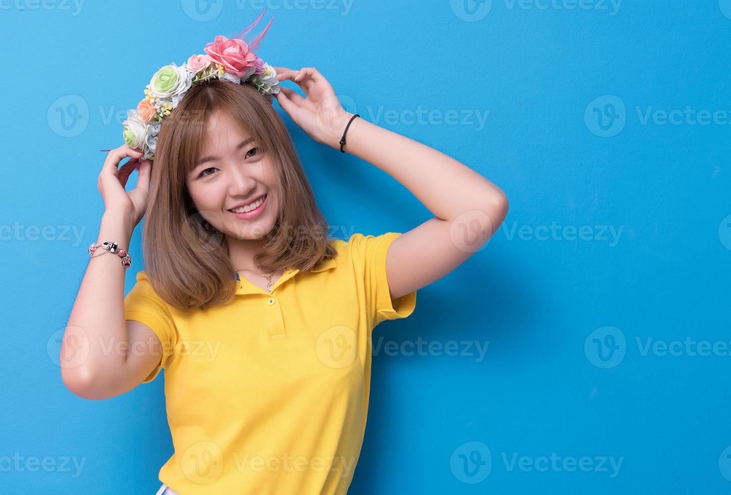 Beauty woman posing with flower hat in front of blue wall background. Summer and vintage concept. Happiness lifestyle and people portrait theme. Cute gesture and pastel tone photo