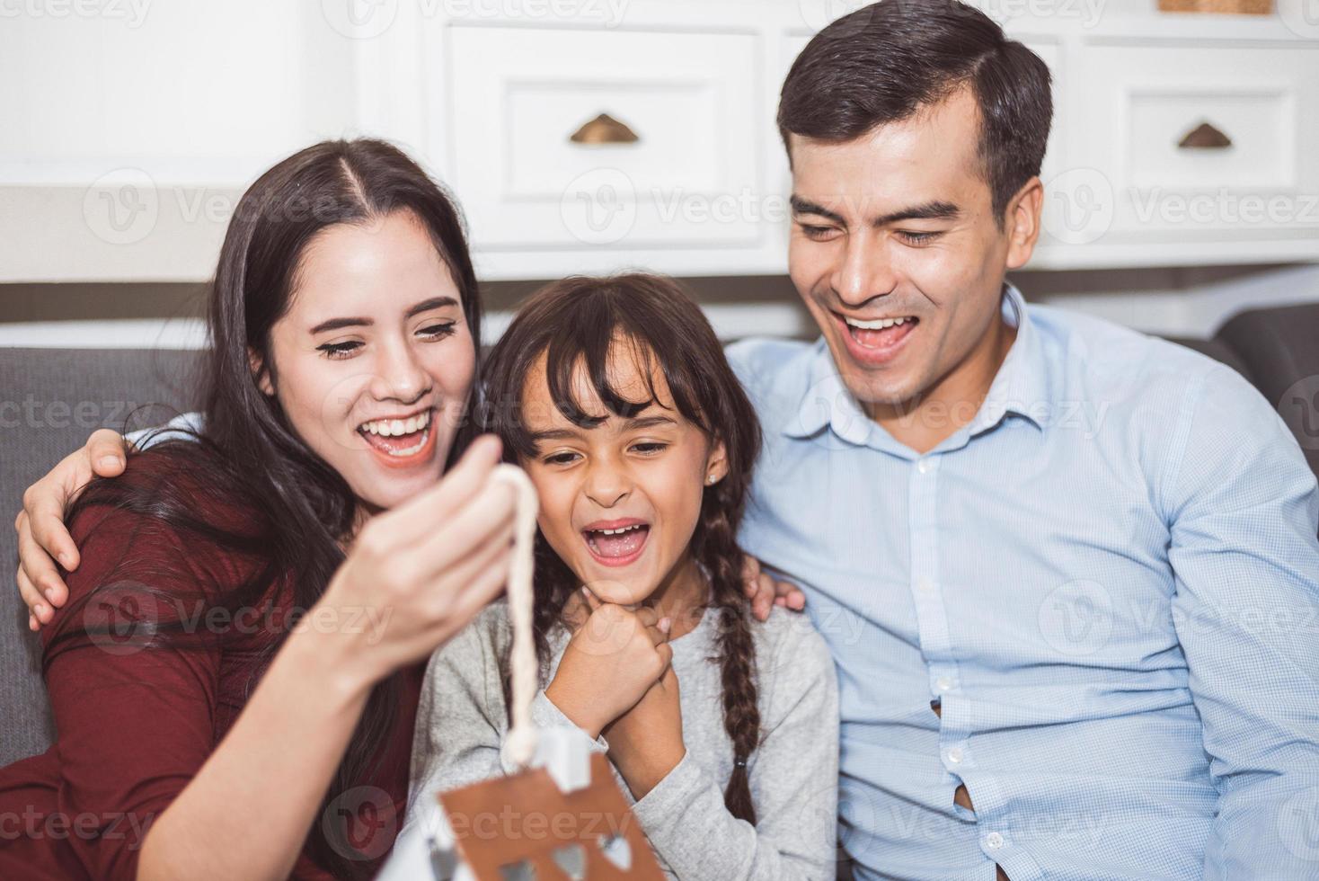 padre y madre sorprenden a su hija con un regalo o un juguete nuevo. padres e hijos son felices juntos en casa en el sofá de la sala de estar. familia y felicidad de la vida concepto foto