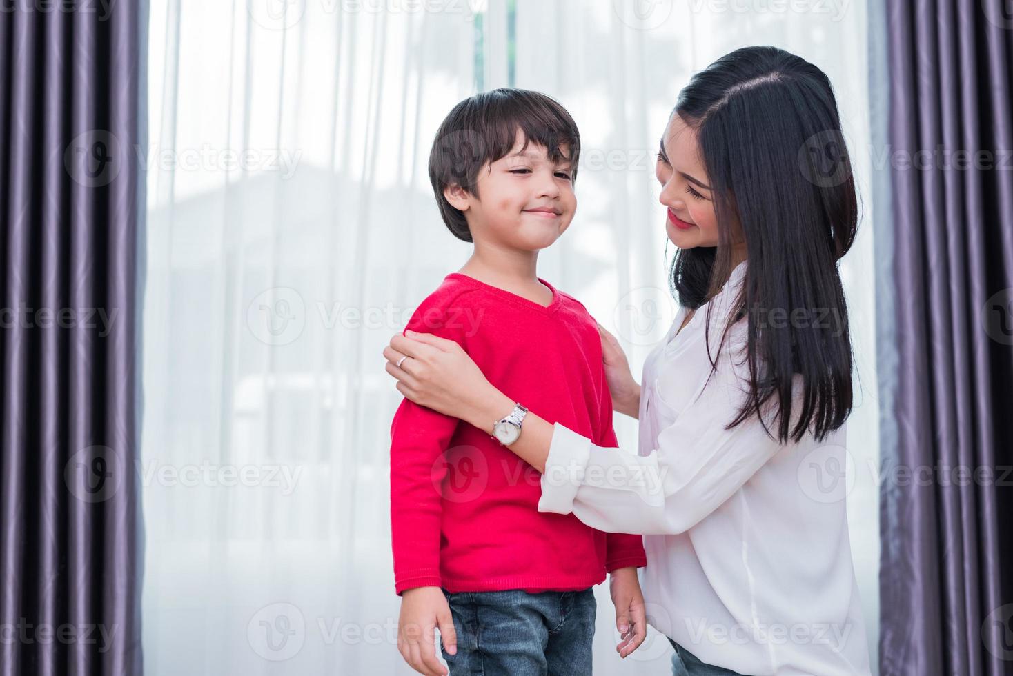 Young Asian mom dressed up son shirt for preparing go to school. Mother and son concept. Happy family and Home sweet home theme. Preschool and Back to school theme photo