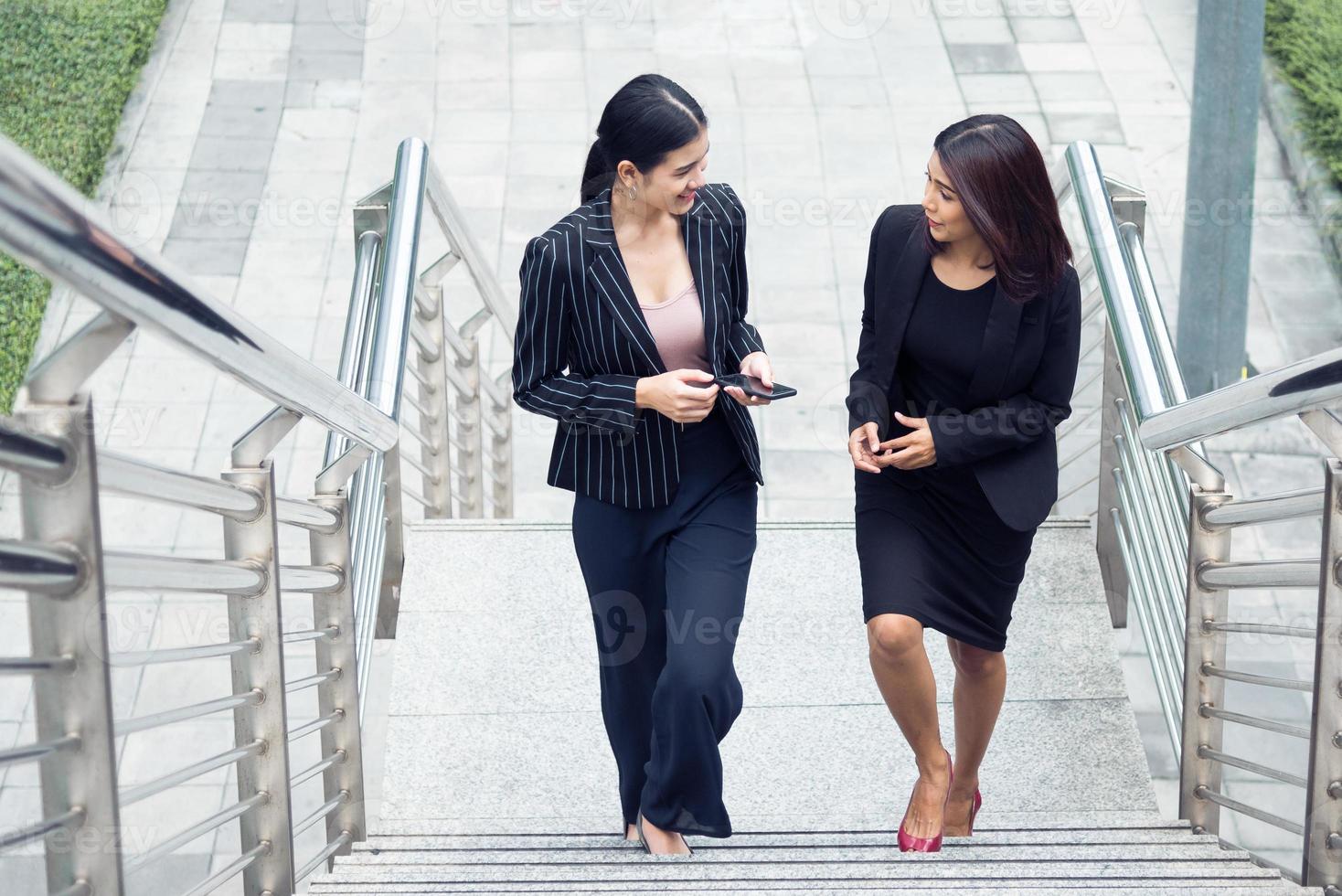 Two businesswomen walking up on stair and talking together. Business and work concept. Job and occupation concept photo