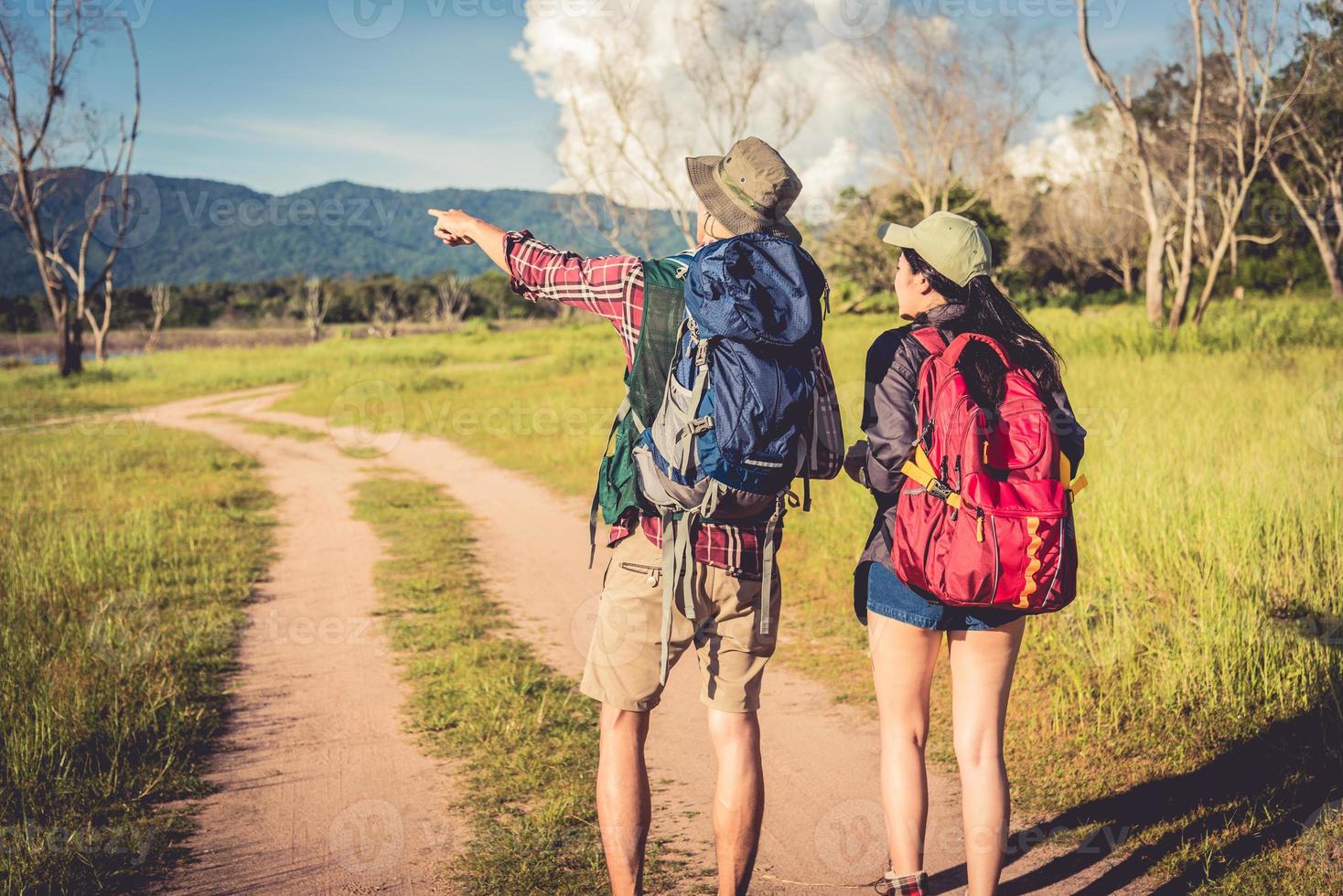 Two people walking on path in meadow field. Male and female traveler looking at attraction view point. Couples adventure at outdoors together. People and lifestyles concept. Trip and camping theme photo