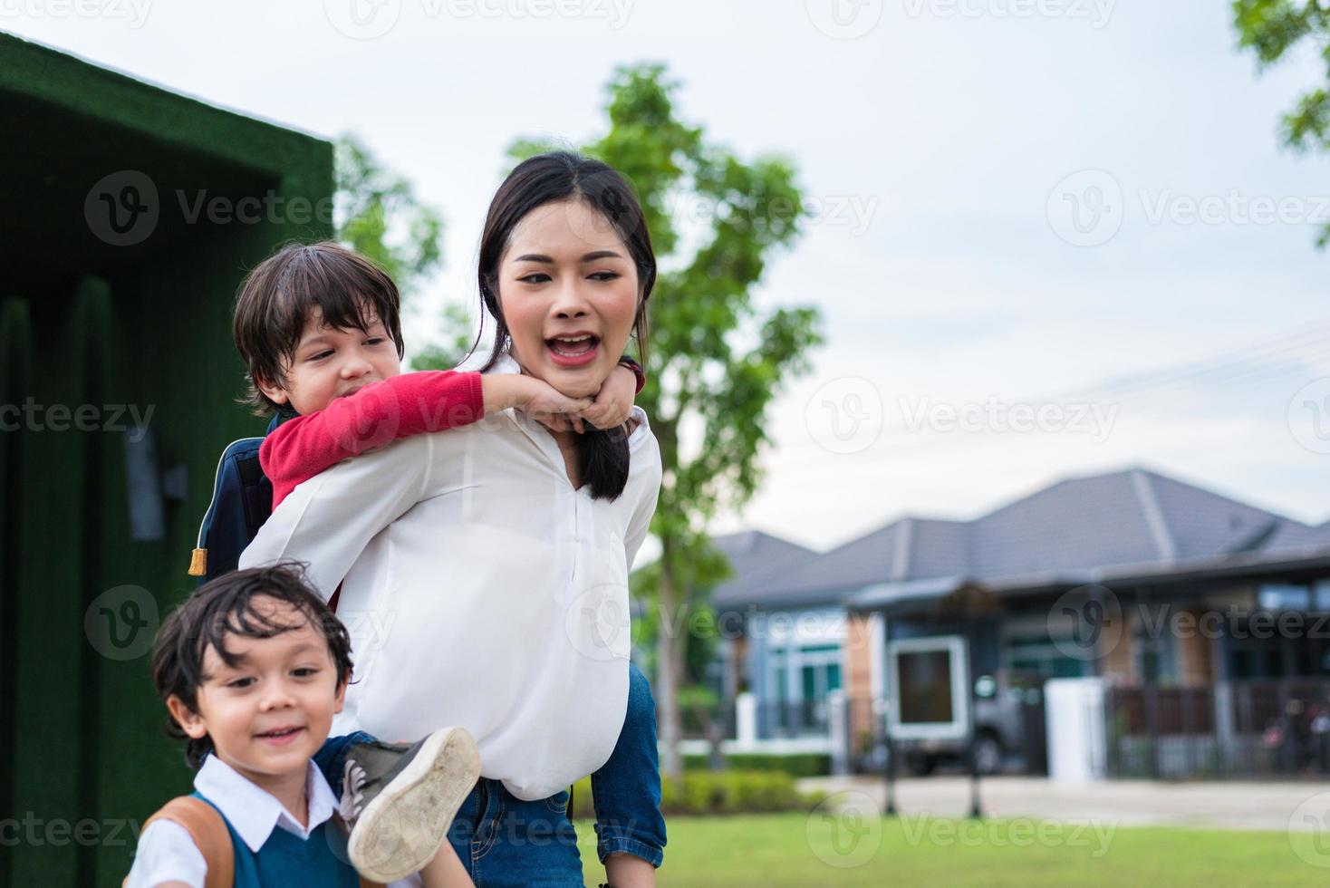 Single mom carrying and playing with her children in  garden with green wall background. People and Lifestyles concept. Happy family and Home sweet home theme. Outdoors and nature theme photo