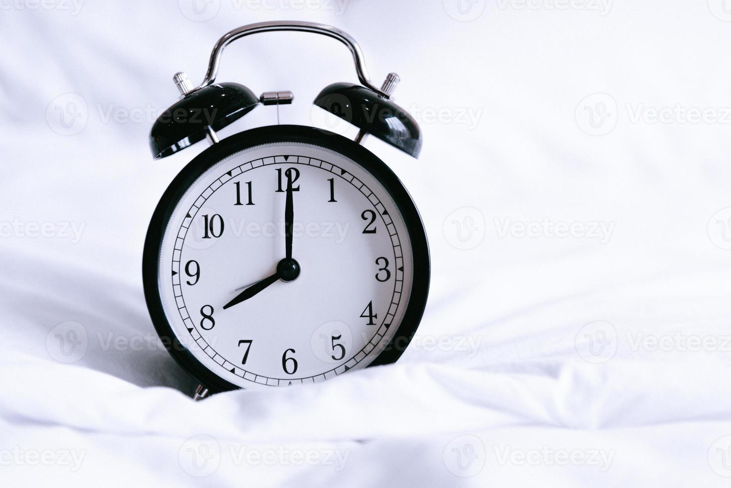 reloj despertador negro en la cama blanca foto