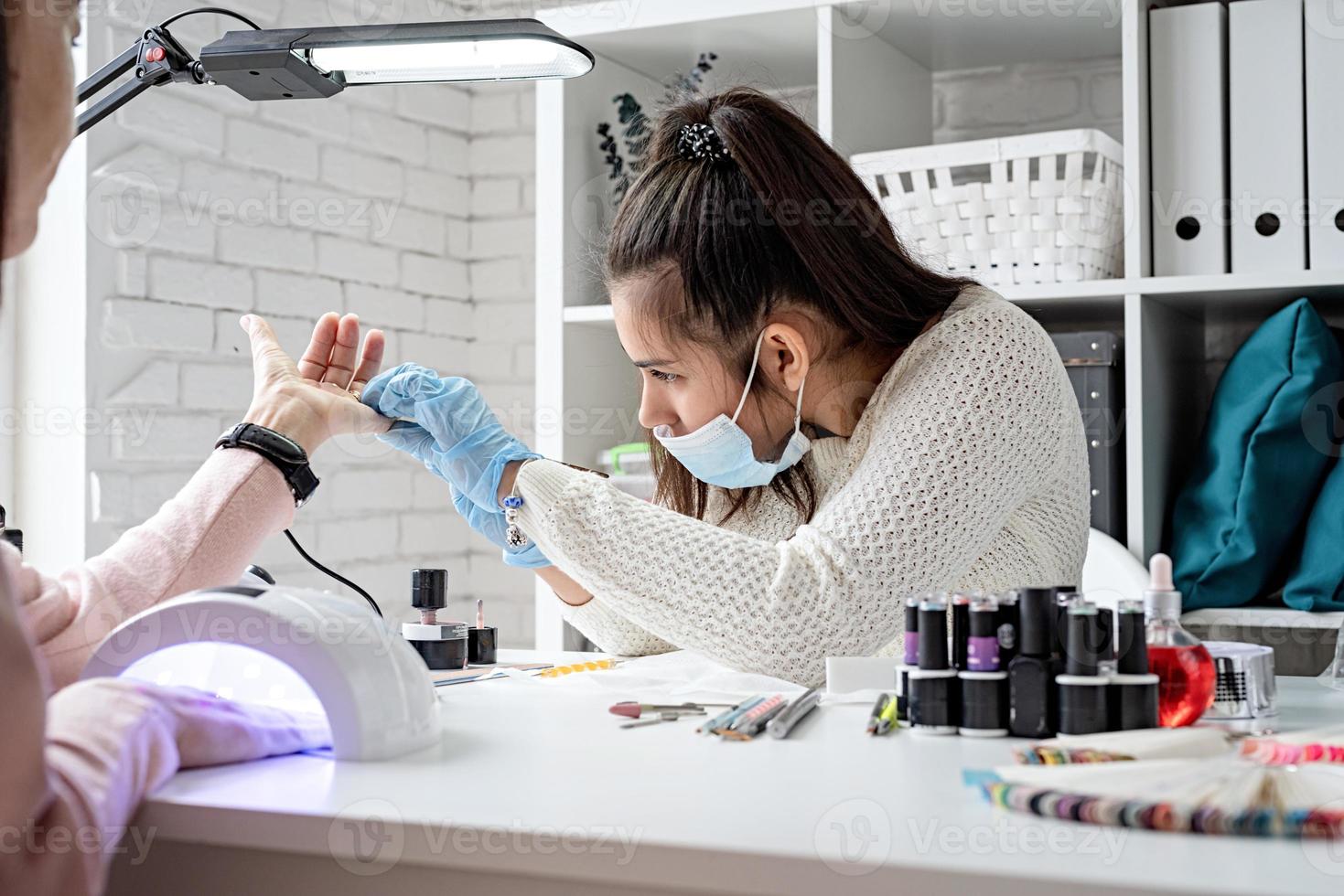 Manicure master in mask and gloves putting on gel polish photo