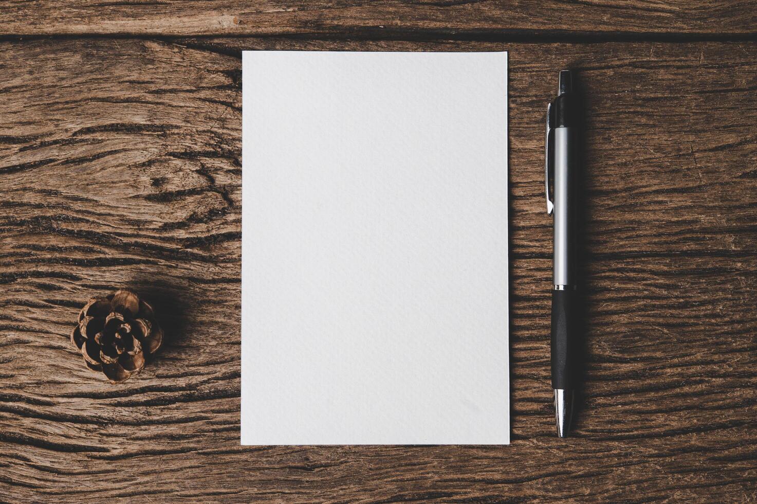 A blank card, pen and Dried pine cones is placed on wood. photo