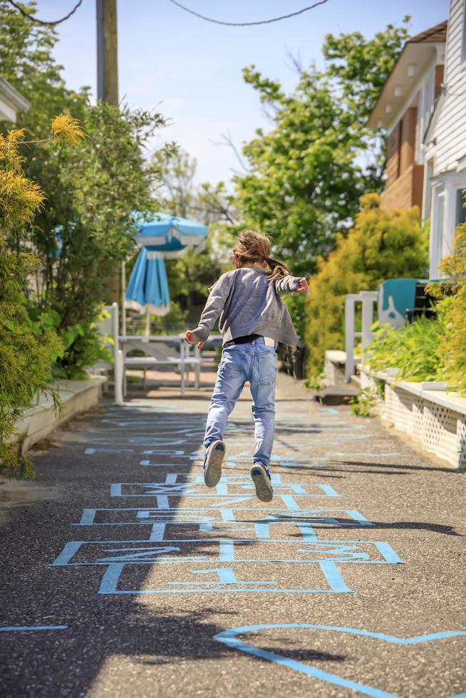 Girl jumping on a hopscotch pattern on a sidewalk in summer photo