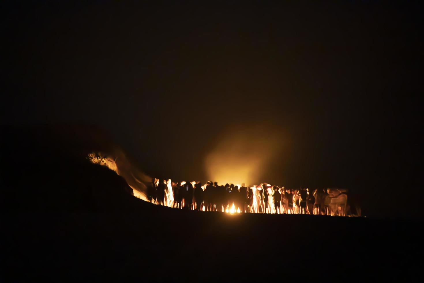 People huddled up near a bonfire on the beach at night photo