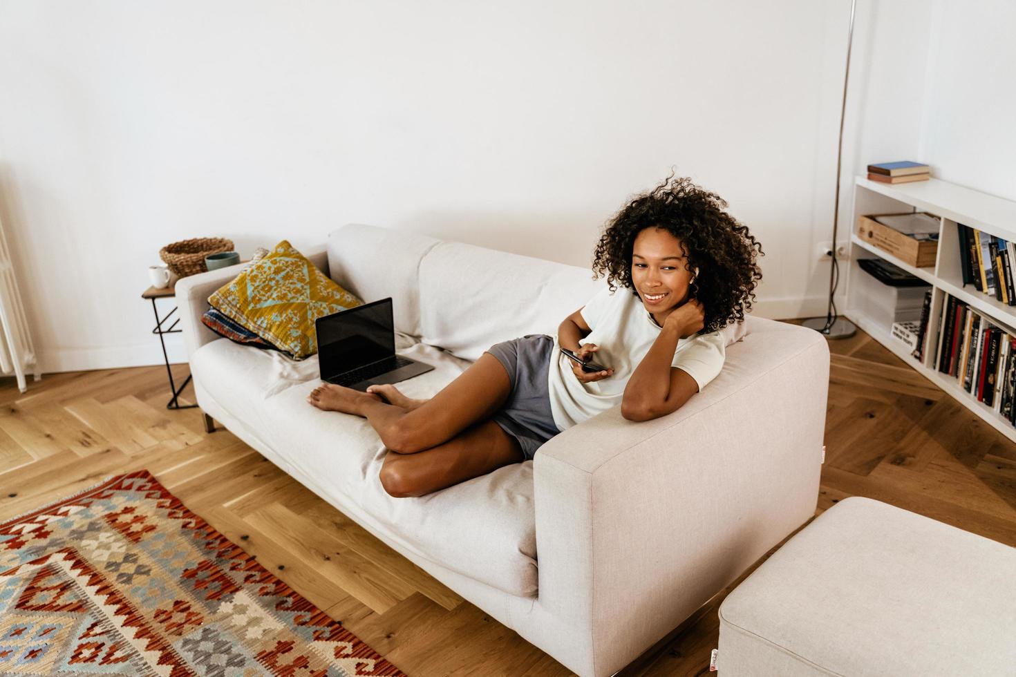 mujer joven negra con teléfono móvil mientras descansa en el sofá foto