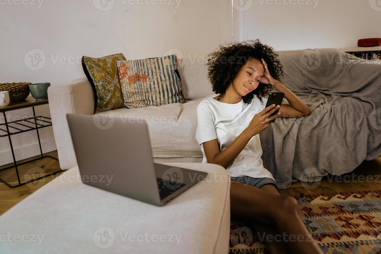 Black young woman uses her mobile phone while sitting on the floor photo